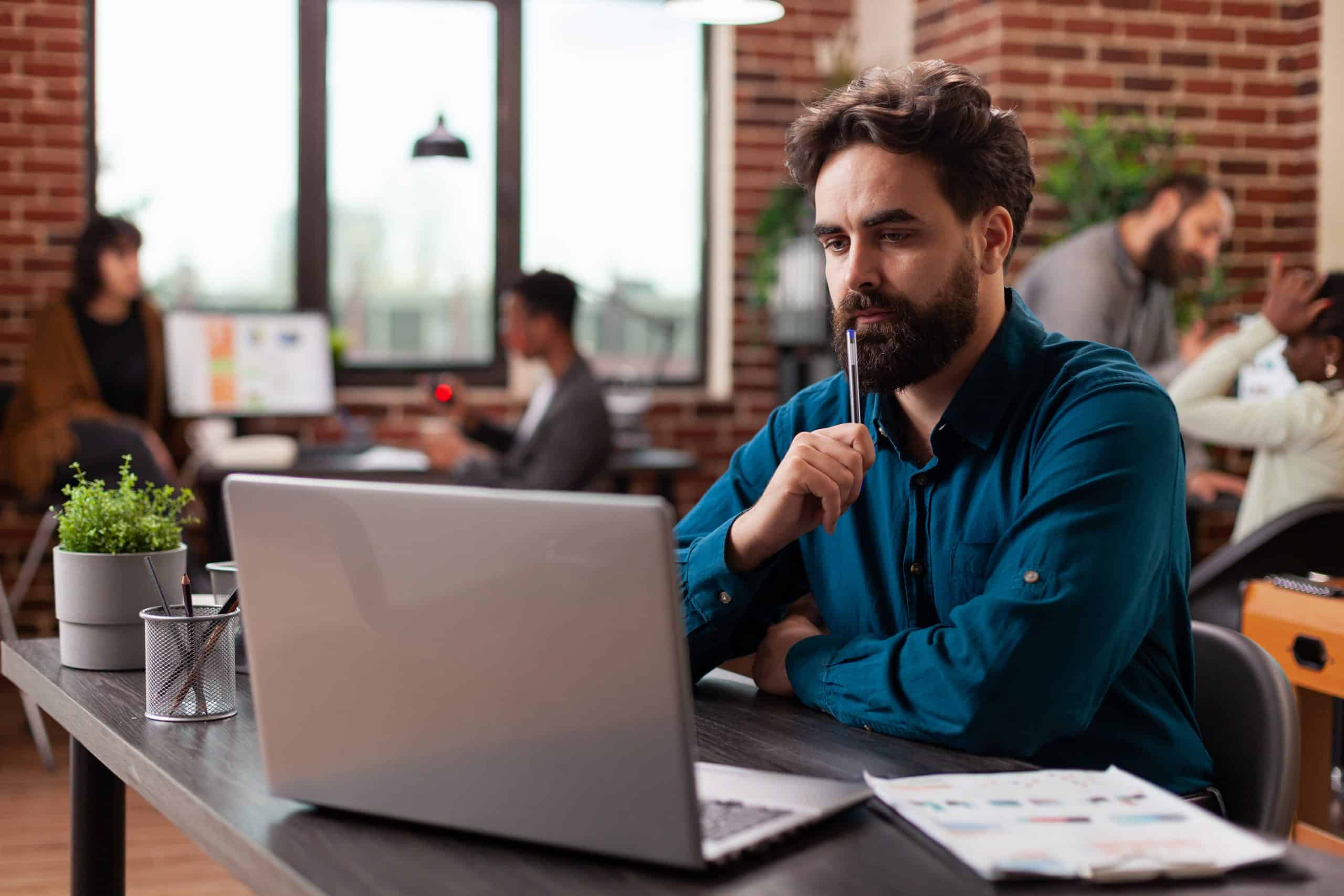 Doubtful pensive entrepreneur having uncertain think about marketing project analyzing company turnover on computer. Businessman working at business collaboration in startup office. Diverse team